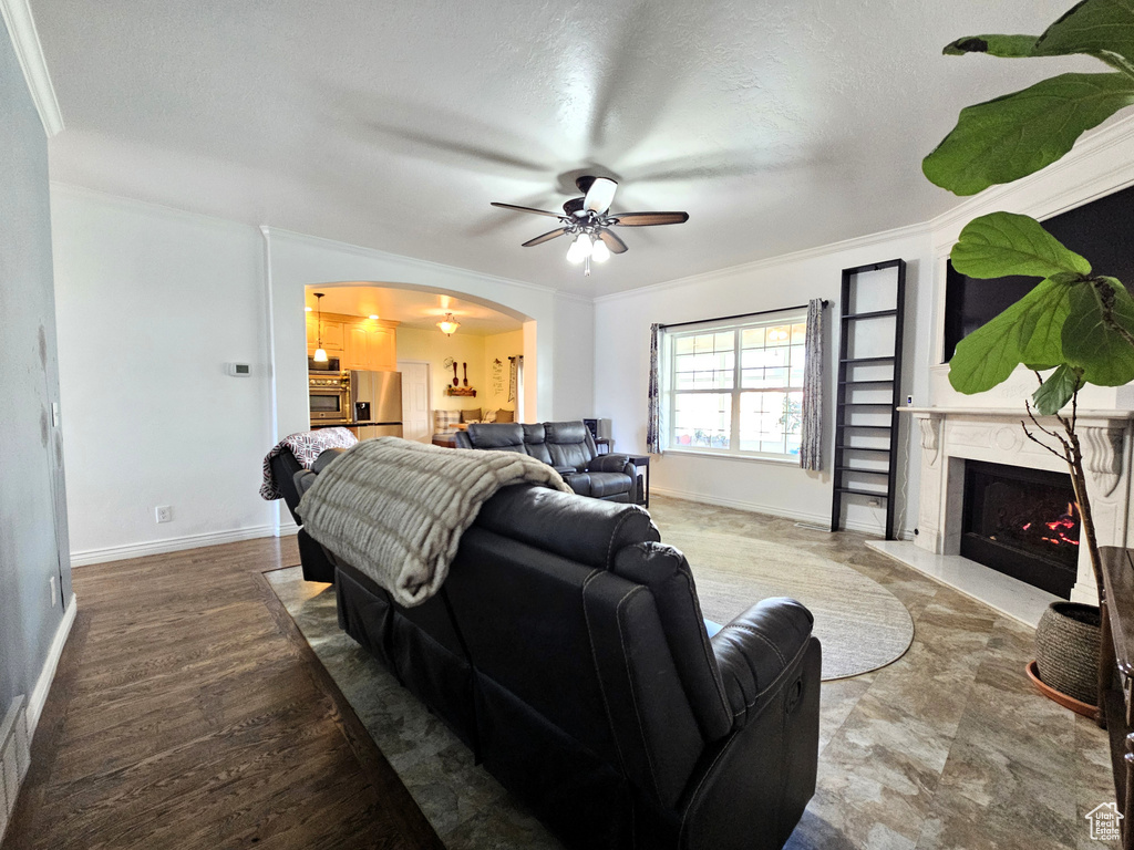 Living area with ceiling fan, arched walkways, a fireplace, baseboards, and ornamental molding