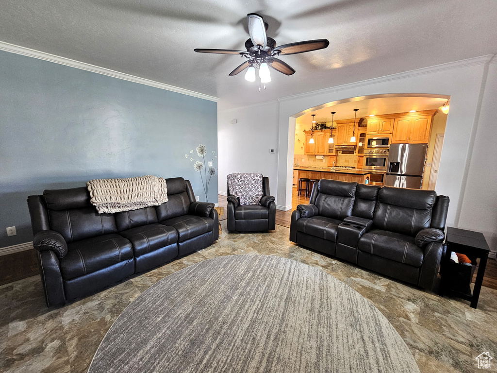 Living area with arched walkways, baseboards, ornamental molding, and a ceiling fan