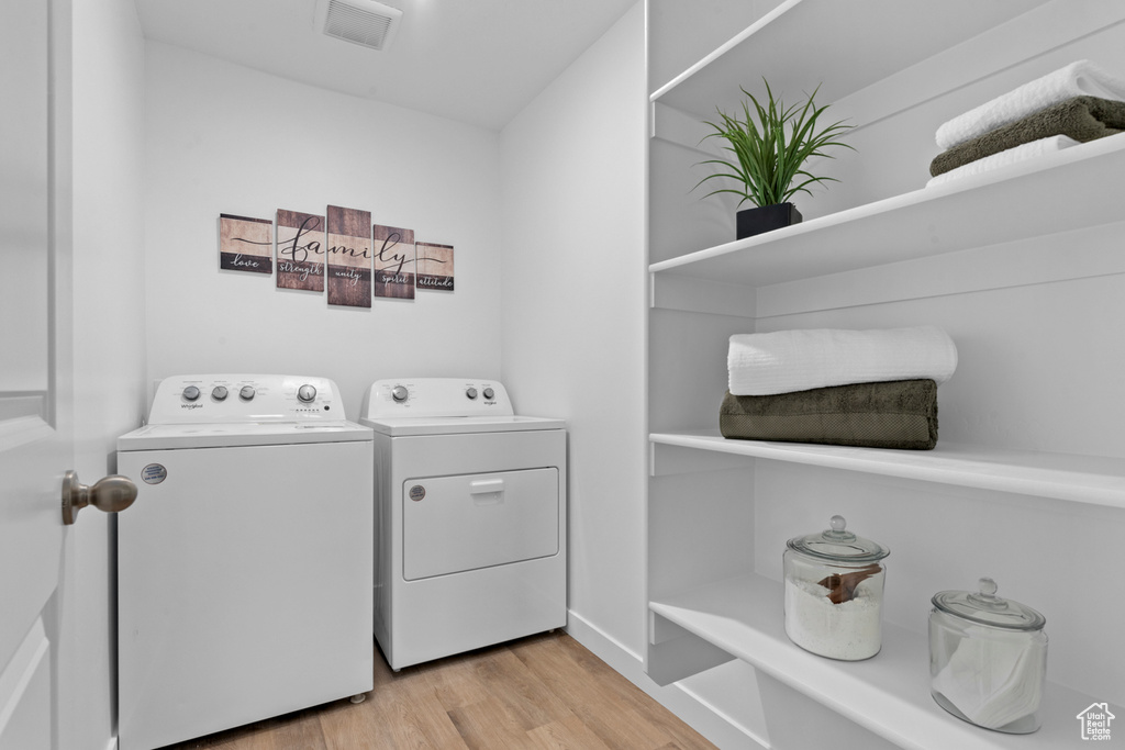 Laundry area with laundry area, washing machine and dryer, light wood-style flooring, and visible vents