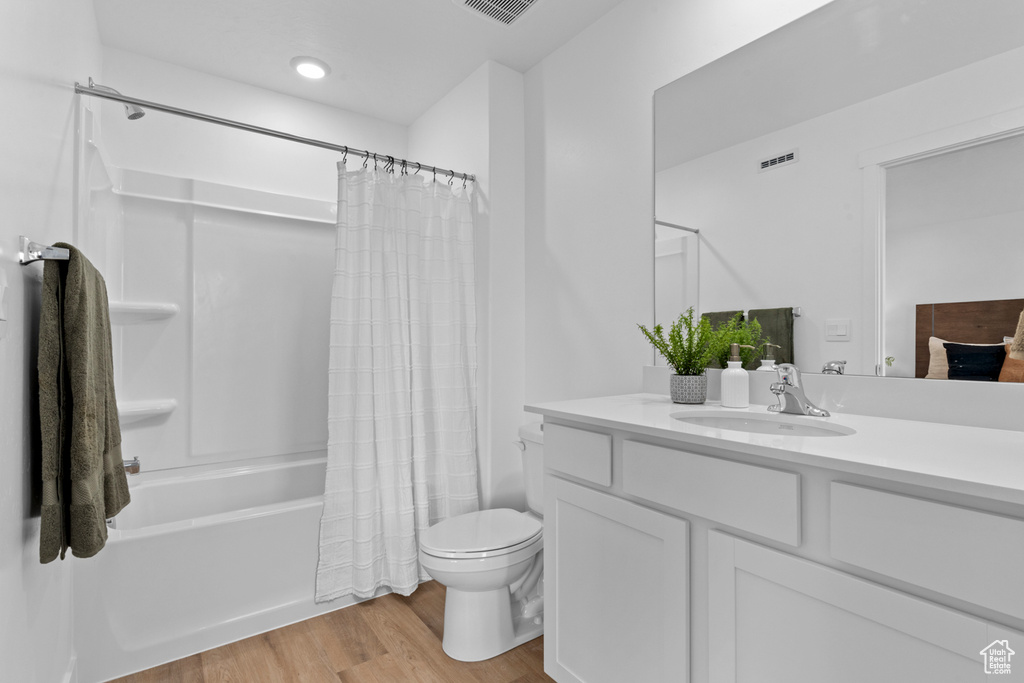 Full bath featuring vanity, toilet, shower / bath combination with curtain, wood finished floors, and visible vents