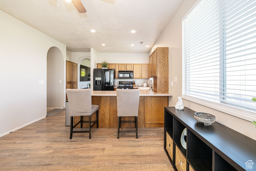 Kitchen with light wood-style floors, a peninsula, black appliances, and ceiling fan