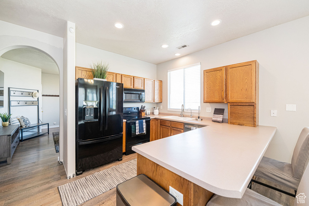 Kitchen with visible vents, a peninsula, light wood-style floors, light countertops, and black appliances