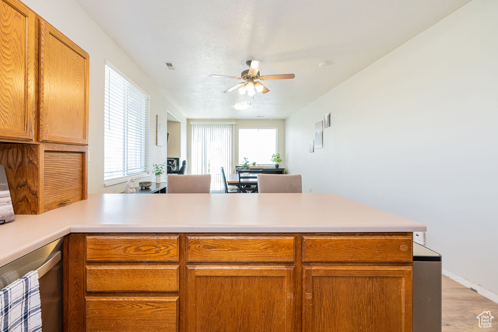 Kitchen featuring ceiling fan, light wood finished floors, light countertops, brown cabinetry, and a peninsula