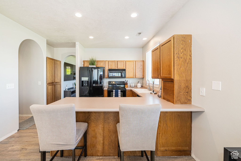 Kitchen with arched walkways, a sink, light countertops, black appliances, and a peninsula