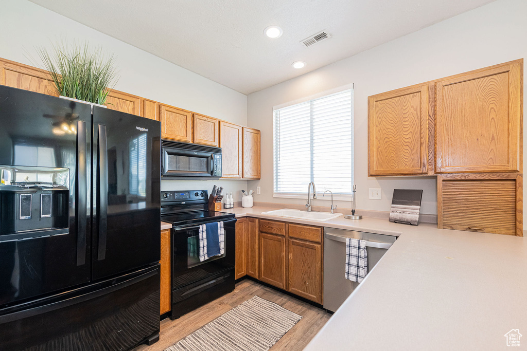 Kitchen featuring visible vents, light countertops, a sink, light wood-style flooring, and black appliances