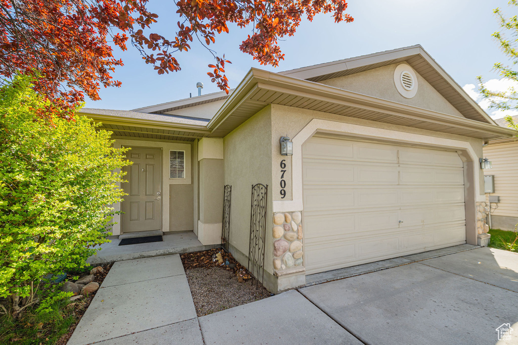 View of front of home with stucco siding, an attached garage, driveway, and stone siding