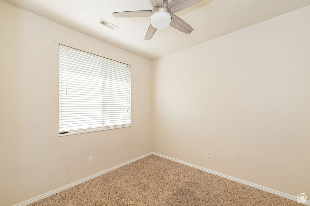 Carpeted empty room featuring visible vents, a ceiling fan, and baseboards