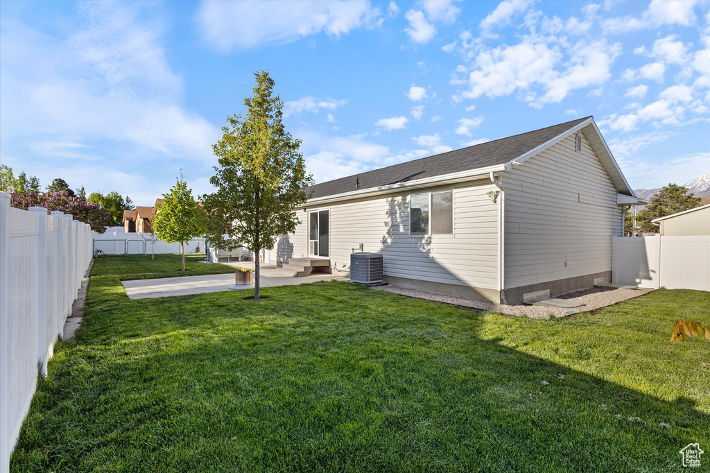 Back of property featuring a lawn, a patio, cooling unit, and a fenced backyard
