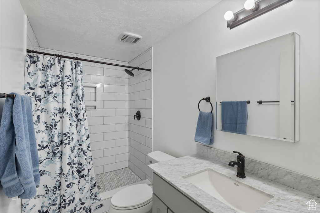 Full bath featuring a textured ceiling, visible vents, vanity, toilet, and tiled shower