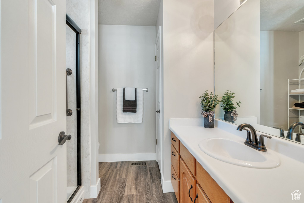 Bathroom featuring a shower with door, wood finished floors, visible vents, vanity, and baseboards
