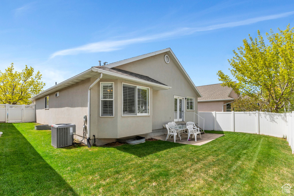 Back of house with central AC unit, a fenced backyard, a yard, stucco siding, and a patio