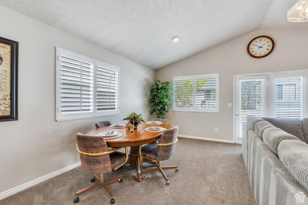 Carpeted dining space with vaulted ceiling and baseboards