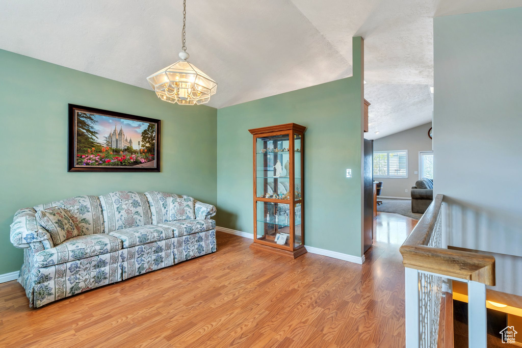 Living room with a textured ceiling, baseboards, a chandelier, lofted ceiling, and wood finished floors