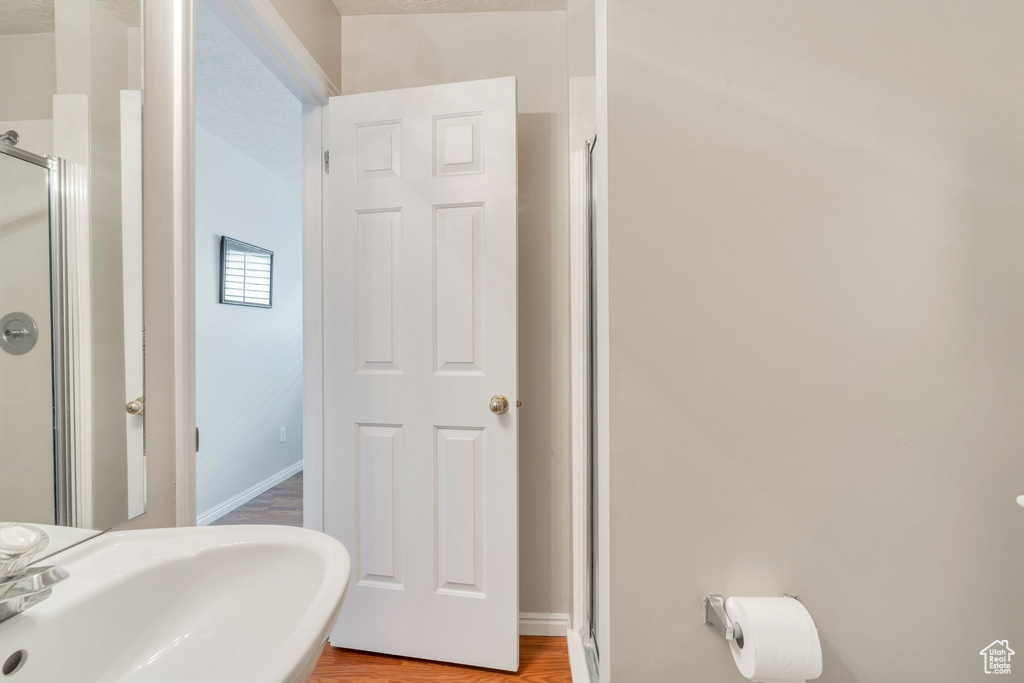 Full bathroom featuring baseboards, wood finished floors, a sink, and a shower stall