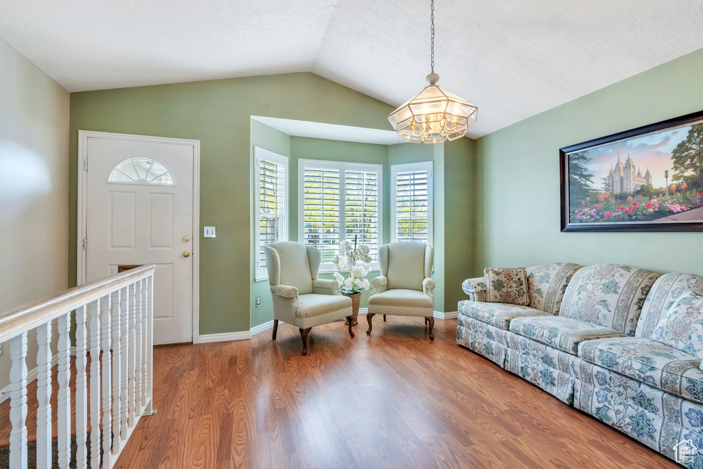Living area with lofted ceiling, baseboards, wood finished floors, and an inviting chandelier