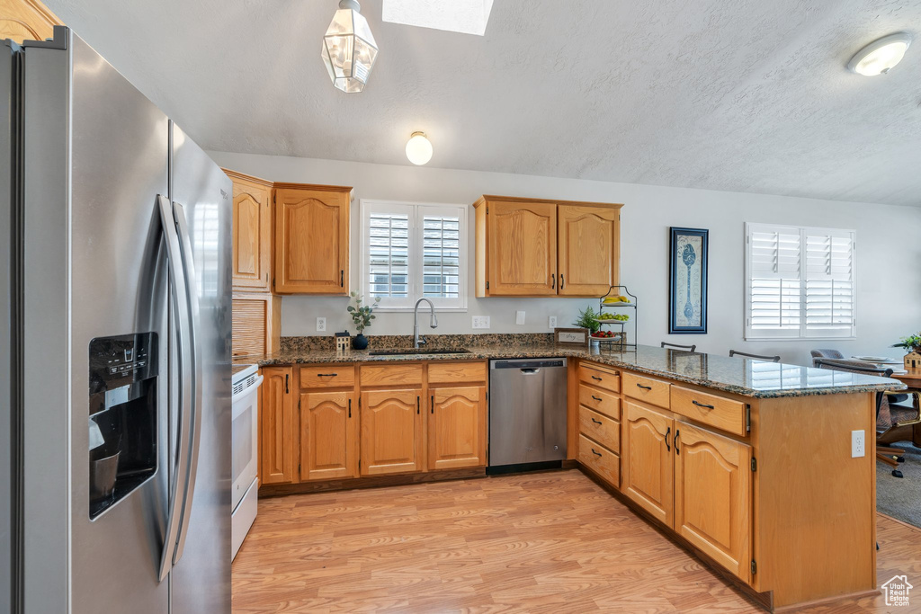 Kitchen with a peninsula, dark stone counters, stainless steel appliances, and a sink