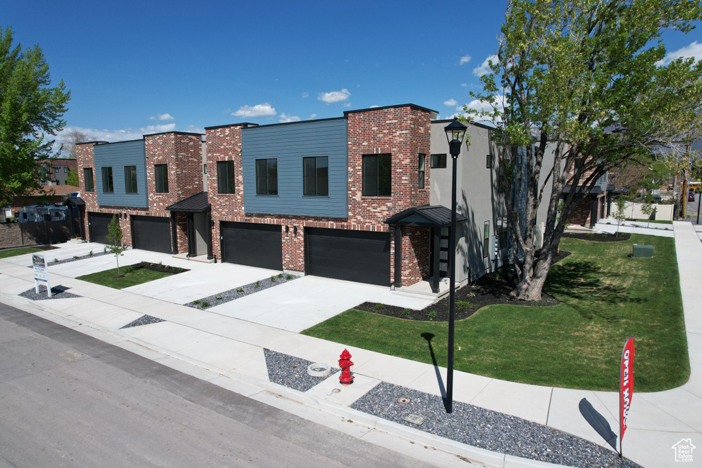 Contemporary house with an attached garage, a front yard, driveway, and brick siding