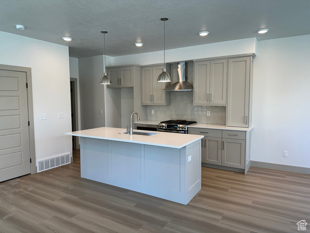 Kitchen with visible vents, stainless steel gas range oven, gray cabinets, wall chimney exhaust hood, and a sink