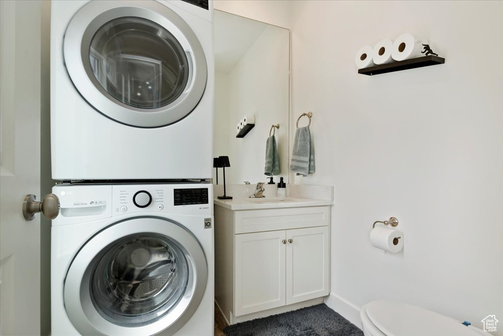 Laundry area with laundry area, a sink, baseboards, and stacked washer / drying machine