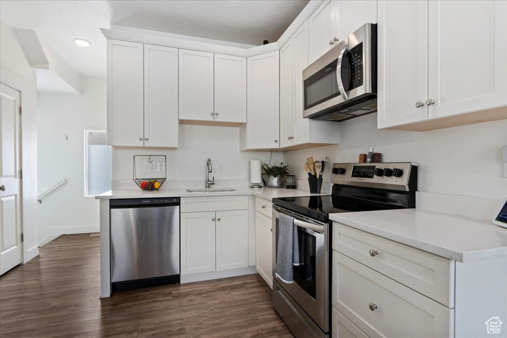 Kitchen featuring a sink, light countertops, dark wood finished floors, stainless steel appliances, and white cabinetry