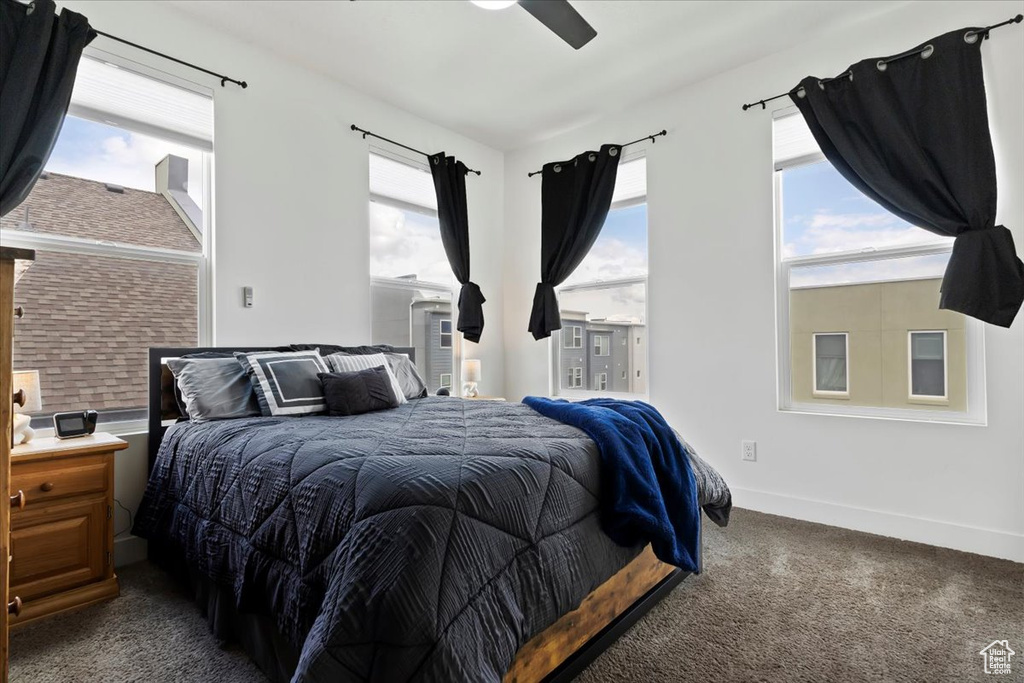 Bedroom with a ceiling fan, baseboards, multiple windows, and dark colored carpet