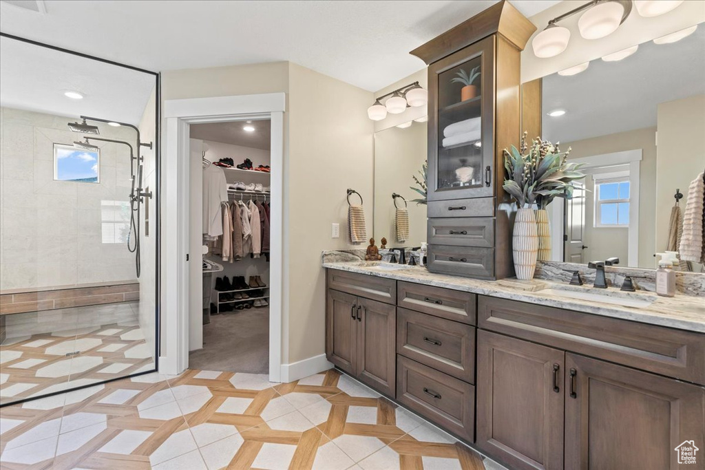 Full bath featuring a tile shower, a sink, double vanity, tile patterned floors, and a spacious closet