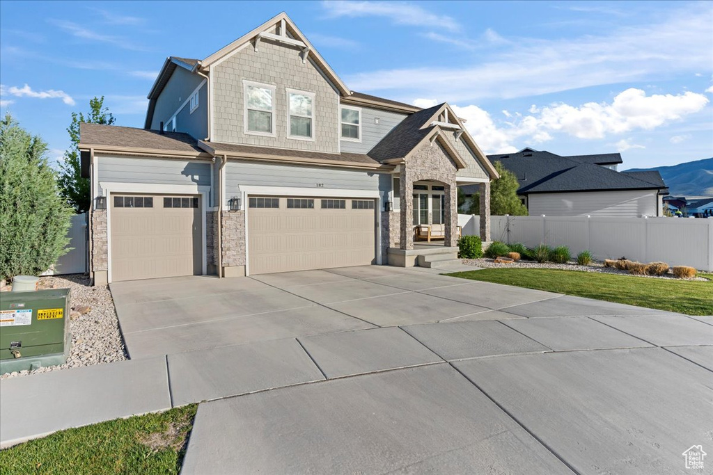 Craftsman-style home featuring fence, stone siding, a garage, a front yard, and concrete driveway