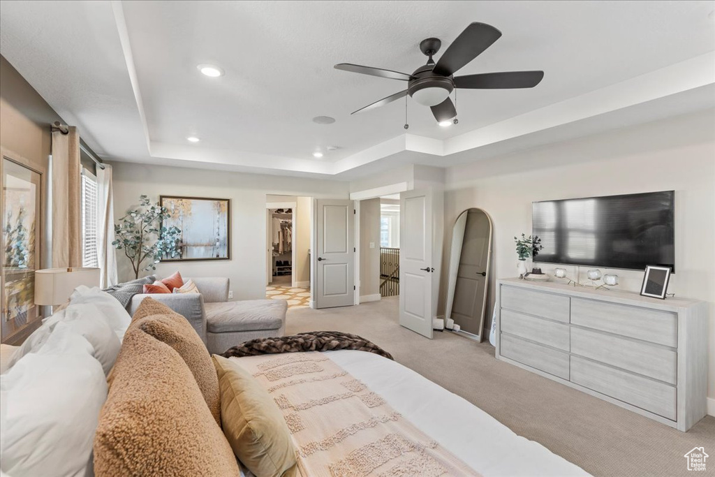 Bedroom with light carpet, a walk in closet, recessed lighting, a raised ceiling, and a ceiling fan