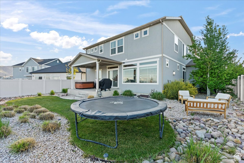 Rear view of house featuring a trampoline, a hot tub, a fenced backyard, a yard, and stucco siding