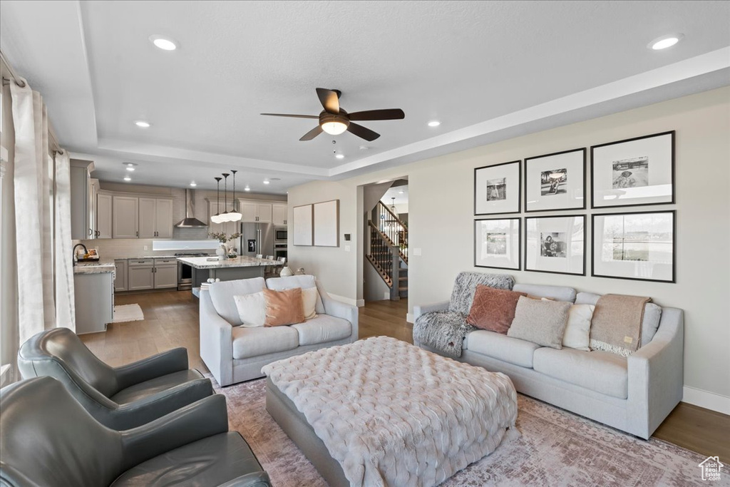 Living room with recessed lighting, a ceiling fan, a raised ceiling, and stairway