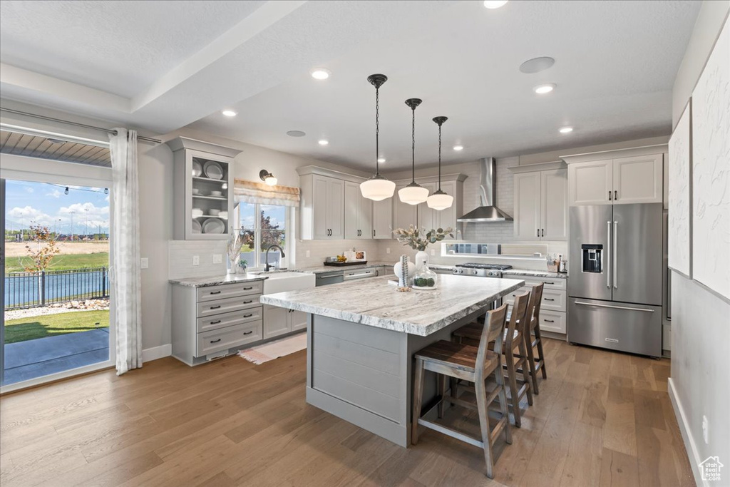 Kitchen with wood finished floors, a breakfast bar area, wall chimney exhaust hood, tasteful backsplash, and appliances with stainless steel finishes