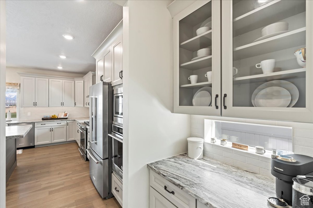 Kitchen featuring tasteful backsplash, light stone countertops, white cabinetry, stainless steel appliances, and light wood-style flooring