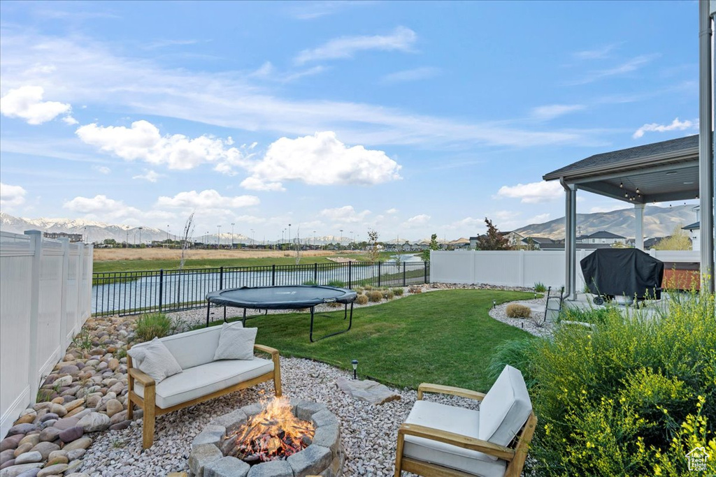 View of yard with a water and mountain view, a fenced backyard, a trampoline, and a fire pit