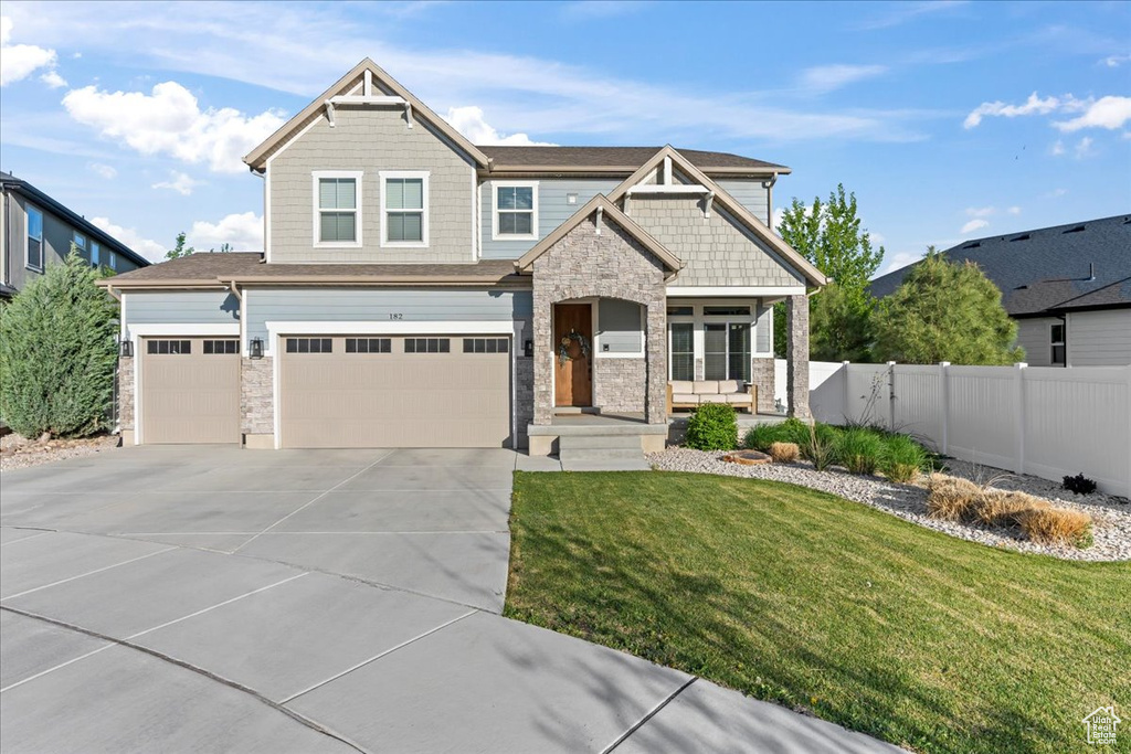 Craftsman house featuring a porch, fence, a front lawn, concrete driveway, and stone siding
