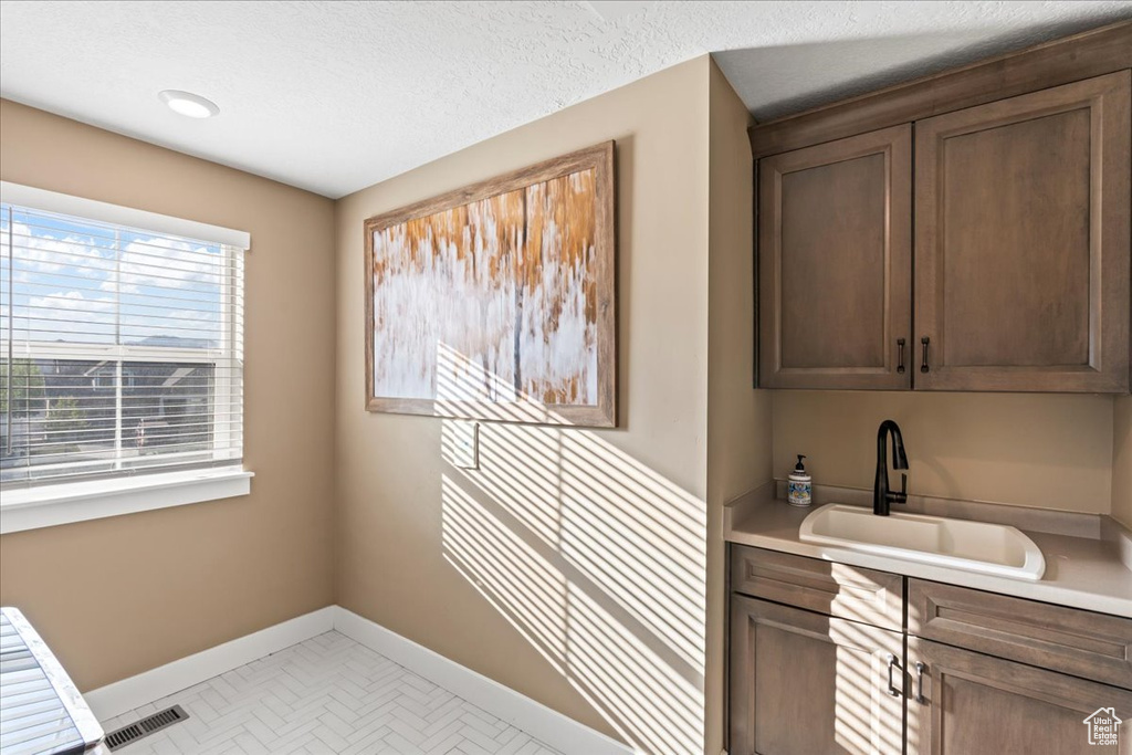 Laundry area featuring a textured ceiling, baseboards, visible vents, and a sink