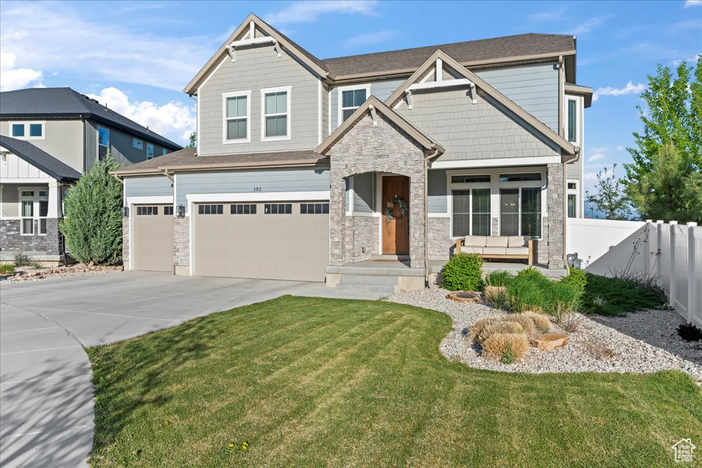 Craftsman house with fence, an attached garage, a front lawn, stone siding, and driveway