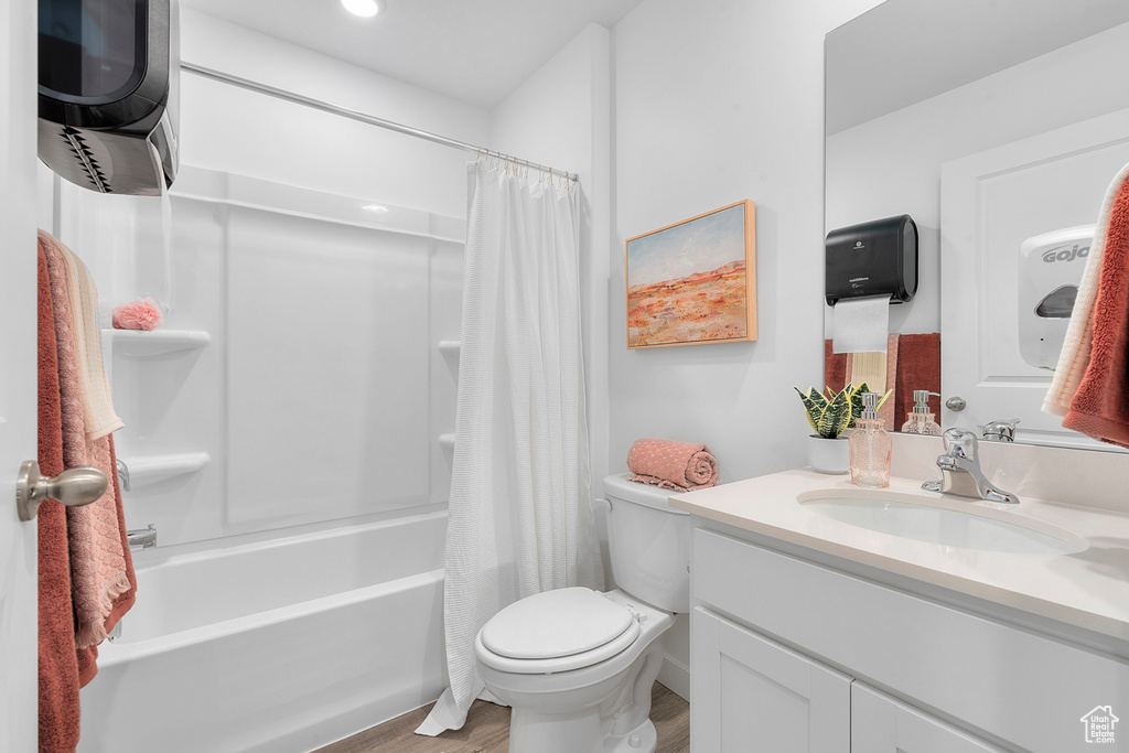 Bathroom with vanity, wood finished floors, shower / bath combination with curtain, and toilet