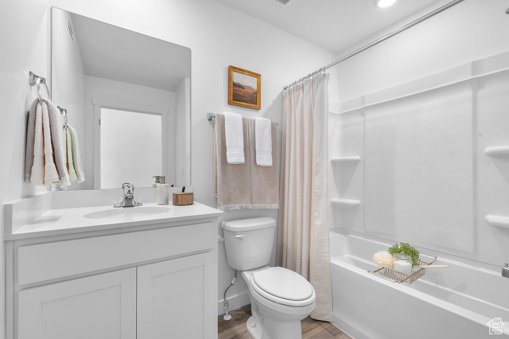 Bathroom with vanity, shower / bath combo with shower curtain, toilet, and wood finished floors