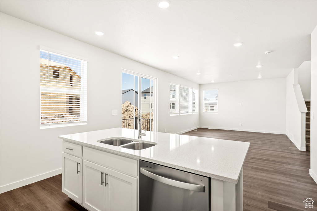 Kitchen with dishwasher, a sink, dark wood-type flooring, a center island with sink, and baseboards
