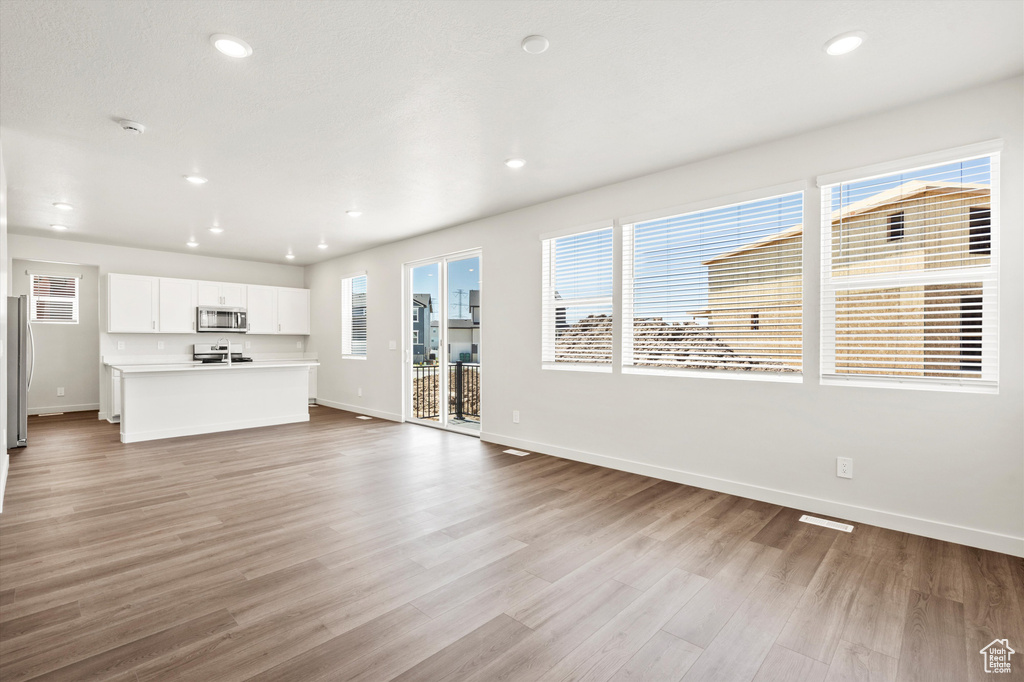 Unfurnished living room featuring baseboards, light wood-type flooring, and recessed lighting