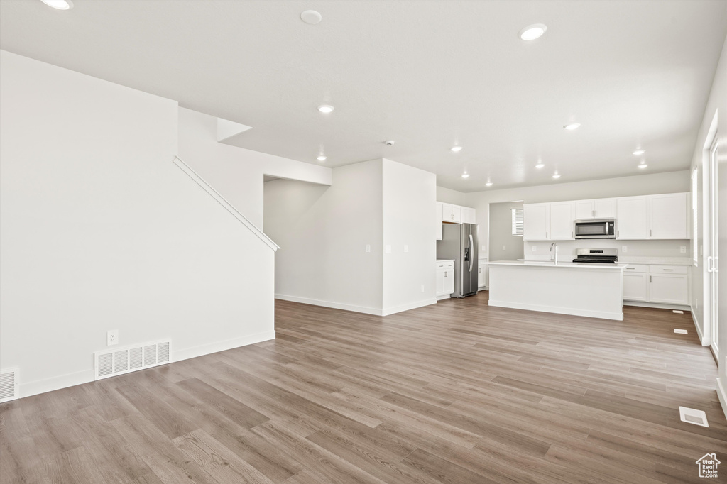 Unfurnished living room with light wood-style flooring, recessed lighting, baseboards, and a sink