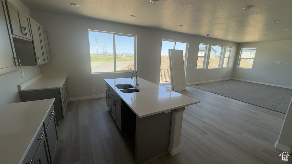 Kitchen with a sink, recessed lighting, baseboards, light wood-type flooring, and a center island with sink