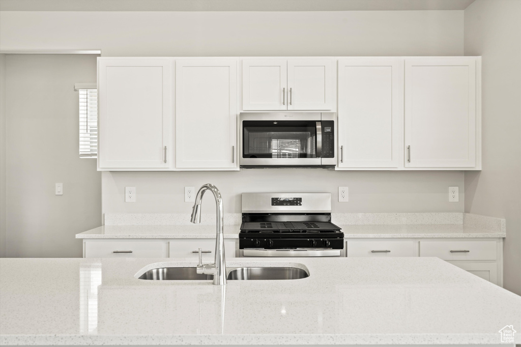 Kitchen with stainless steel appliances, white cabinetry, a sink, and light stone countertops