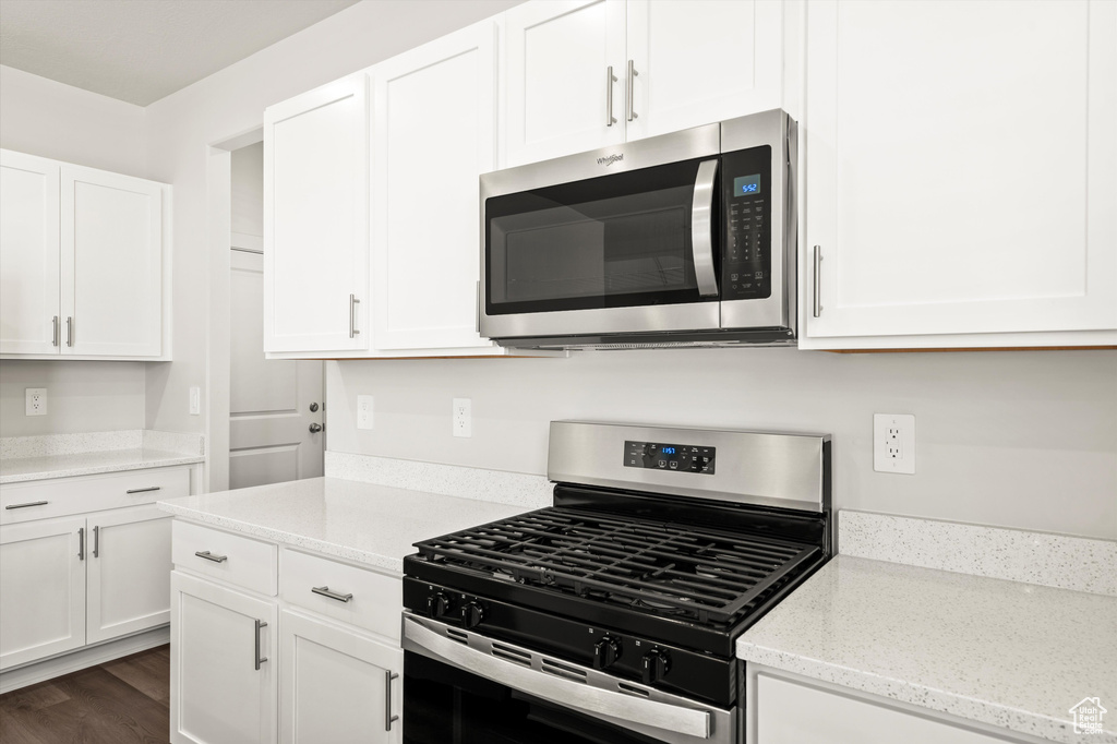 Kitchen featuring stainless steel appliances, white cabinetry, and light stone countertops
