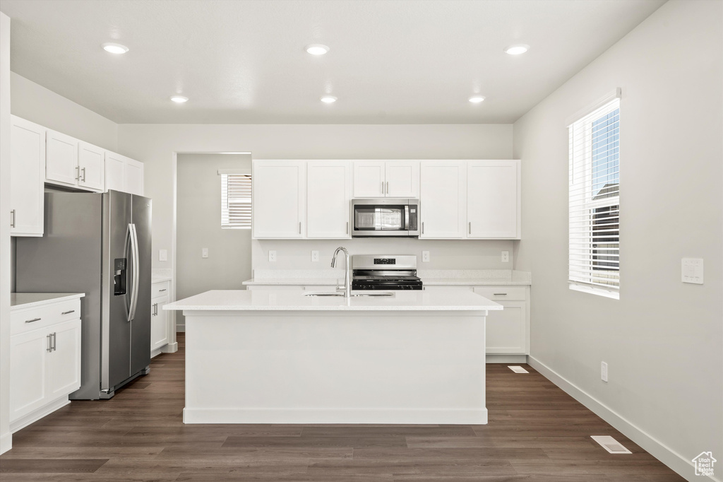 Kitchen with appliances with stainless steel finishes, a sink, an island with sink, white cabinetry, and light countertops