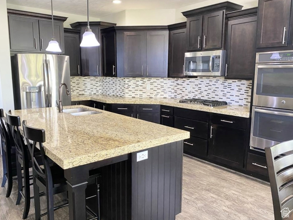 Kitchen with a sink, light stone counters, stainless steel appliances, and light wood-style flooring