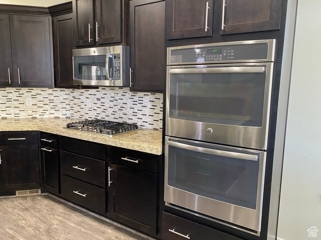 Kitchen with light stone counters, appliances with stainless steel finishes, backsplash, and dark brown cabinetry