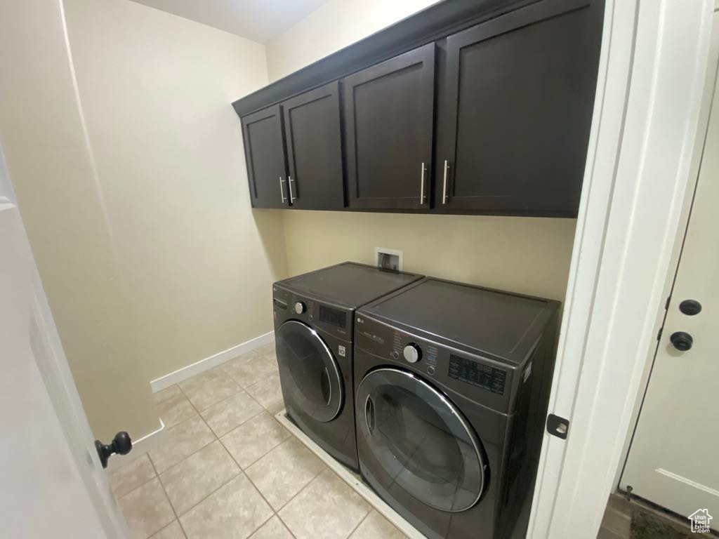 Laundry area with light tile patterned floors, baseboards, cabinet space, and independent washer and dryer