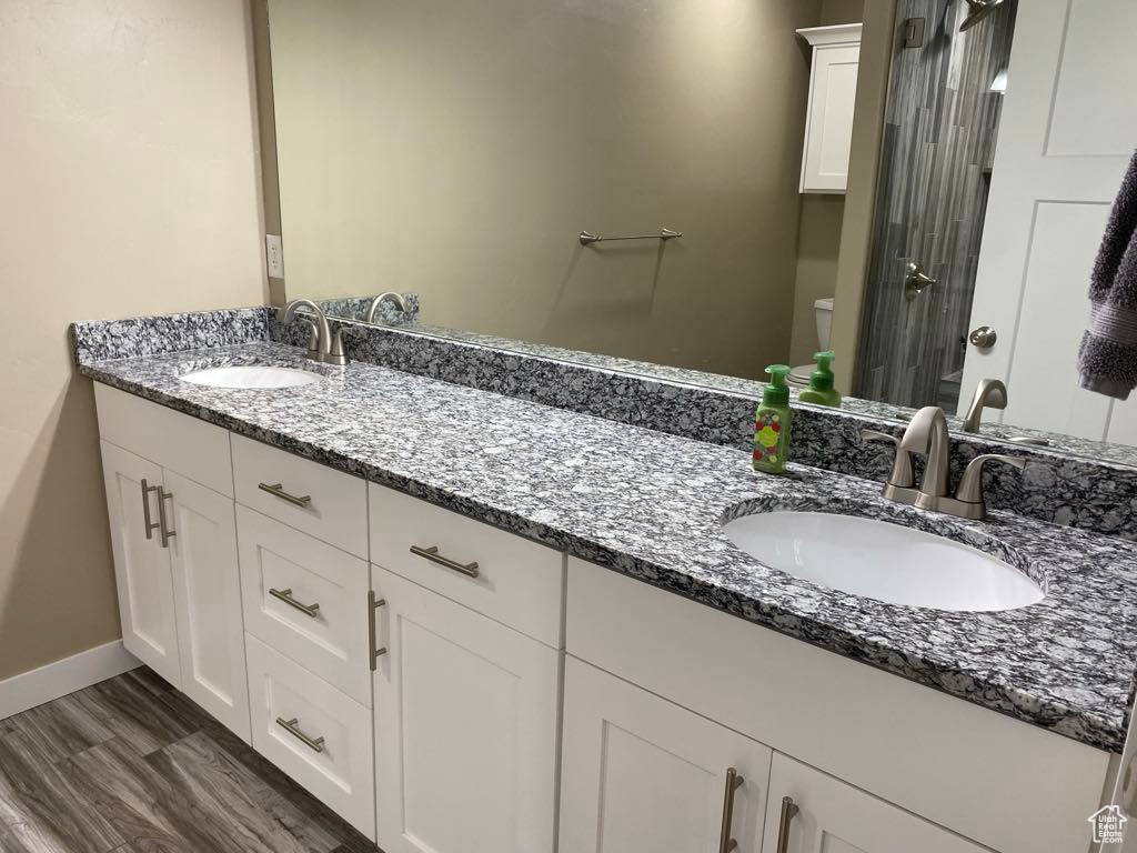 Bathroom featuring baseboards, double vanity, toilet, and a sink