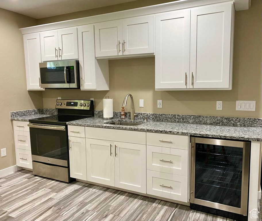 Kitchen featuring light wood-style floors, appliances with stainless steel finishes, a sink, and wine cooler
